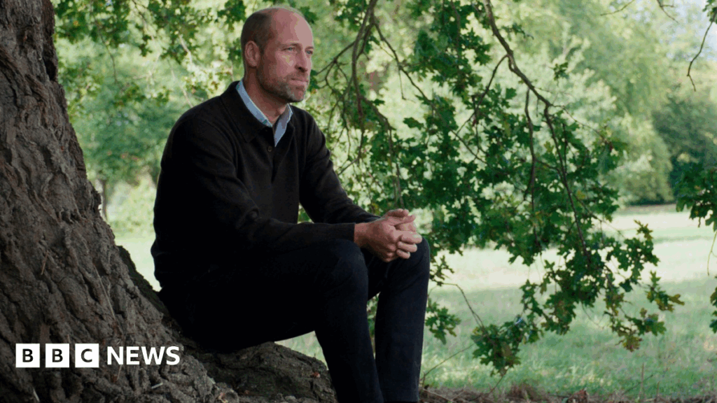 Prince William sits at the foot of a tree looking out beyond the shot of the camera.
