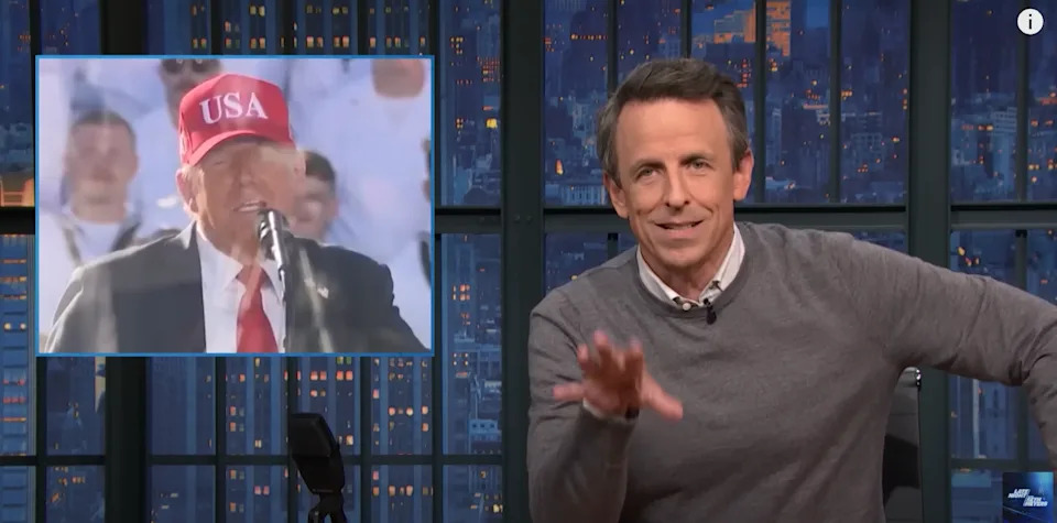 A TV show host gesturing during a segment with an inset showing a man in a hat speaking at a podium