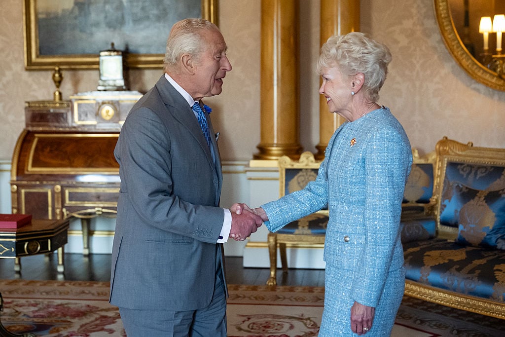 Two people shake hands while standing in the middle of a room.