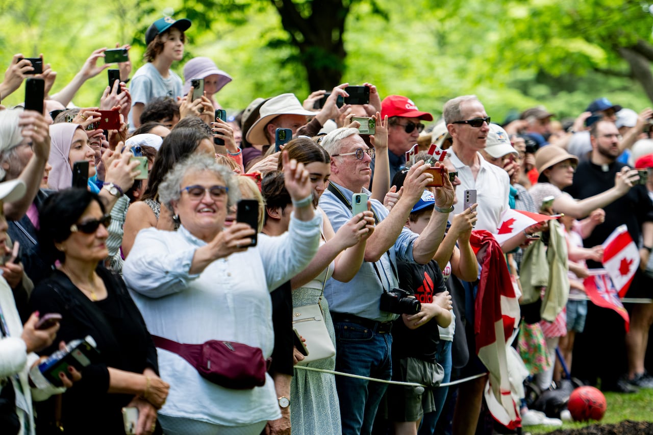 Visitors to a tree planting ceremony try to catch a glimpse of  King Charles and Queen Camilla, both not seen, as they arrive to the grounds of Rideau Hall in Ottawa, on Monday, May 26, 2025.