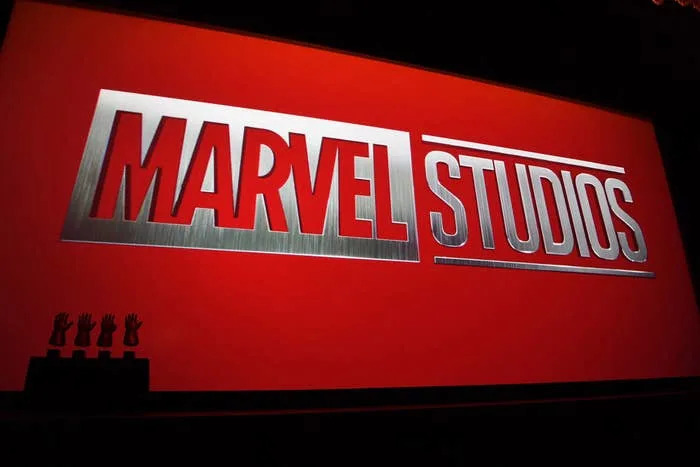 Marvel Studios logo displayed on a large screen at a media event, with small trophy silhouettes visible below
