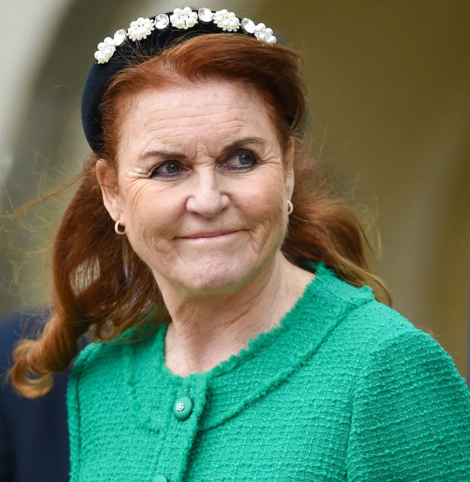  Sarah Ferguson wearing a green jacket and black headband looking to the side and smirking. 