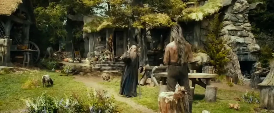 Two figures in a rustic, medieval-style garden with stone buildings, surrounded by lush greenery and animals