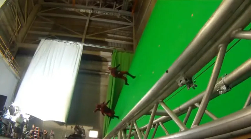 Two stunt performers in harnesses fly against a green screen backdrop on a film set, simulating an action scene