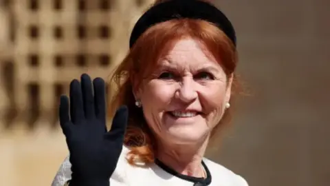 EPA Sarah Ferguson is wearing a black glove and waving towards the camera. She has a small black hat on her head and her red hair is long and pulled away from her face. She is wearing a white dress with a small black collar at the neck and a pair of pearl earrings.