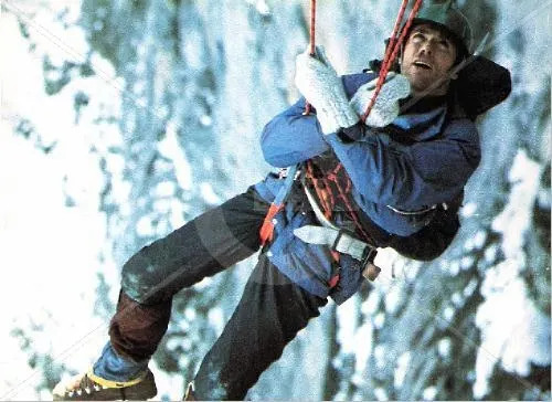 A climber suspended mid-air with ropes, wearing protective gear and gloves, against a snowy mountain background