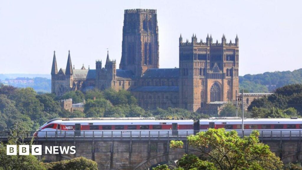 Durham Cathedral to mark railway 200th anniversary A grey and red LNER train passing on a viaduct on its way to Durham station. The line overlooks Durham Cathedral. It is a large stone building with several towers and intricate ornaments.
