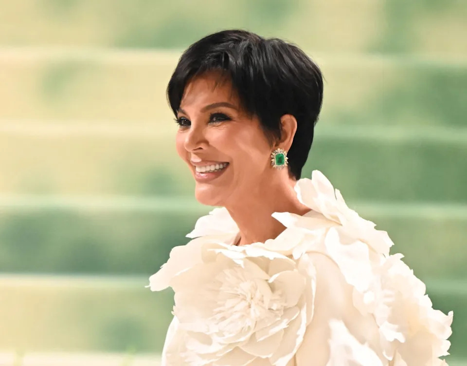 Person smiling in a floral outfit with large, textured flowers on the shoulders, looking elegant at a formal event