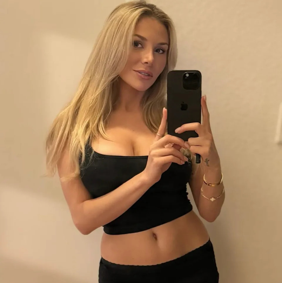 Courtney Stodden taking a selfie in a mirror, wearing a fitted top, with long hair styled down