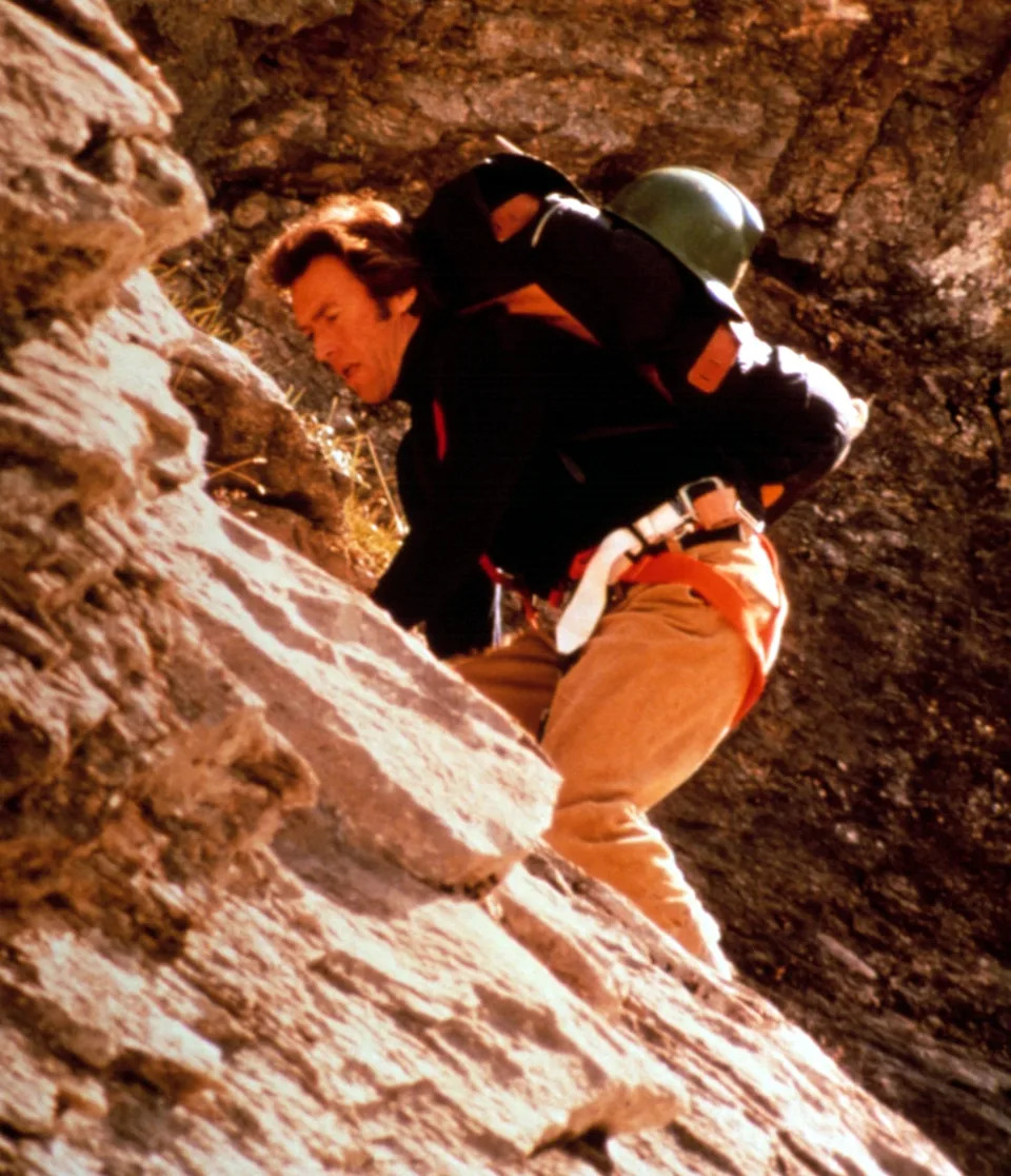 A person with a backpack is rock climbing on a steep, rocky surface, focused and in motion
