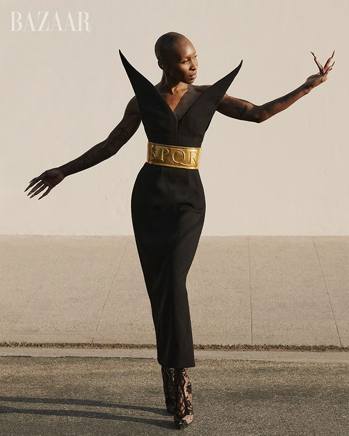 Cynthia Erivo posing in a sculptural black dress with a gold belt, striking an expressive pose in a high-fashion shoot.