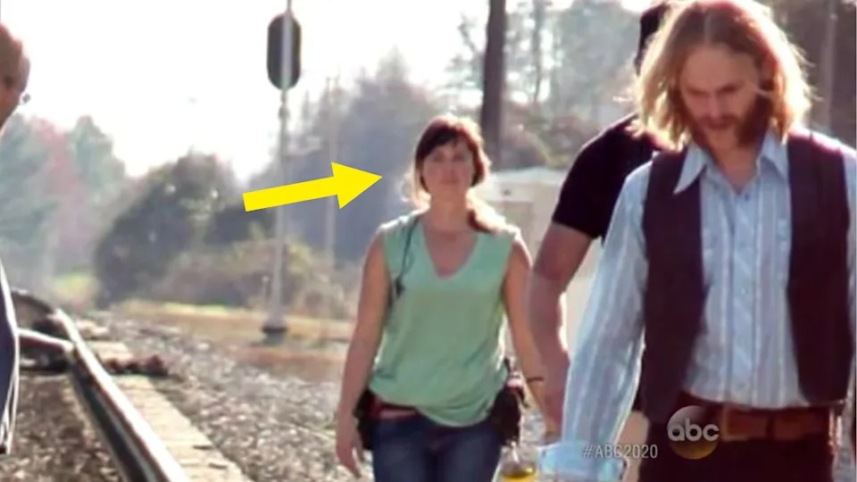 A person walking on a railway track is highlighted with an arrow; others walk nearby