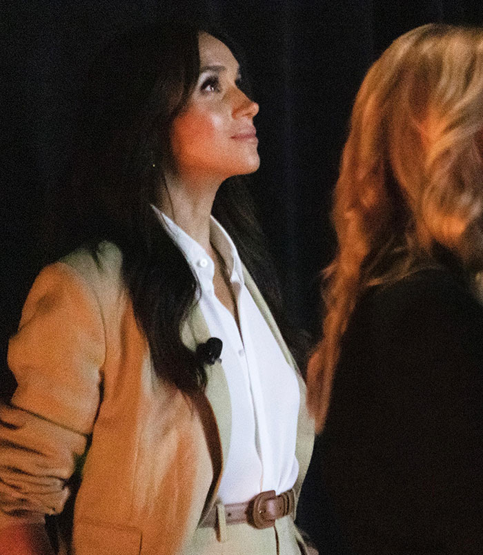 Woman in beige suit and white shirt looking upward, related to Meghan Markle backlash and Lana Del Rey's husband praised.