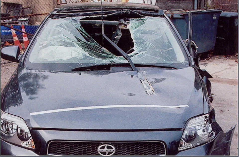 Car with shattered windshield and damaged roof, parked outdoors