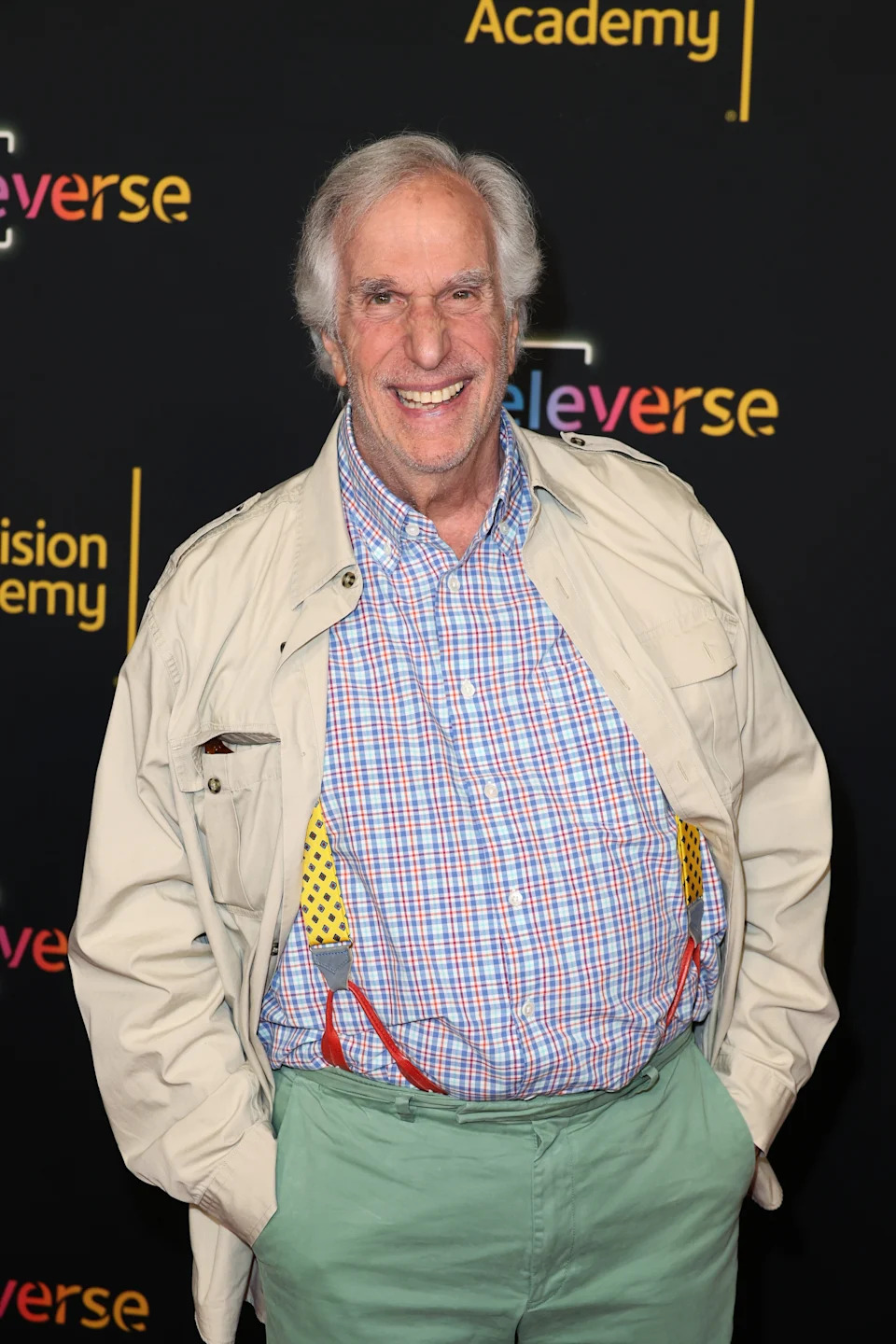 Man in a checkered shirt, light jacket, and suspenders smiling at an event for the Television Academy