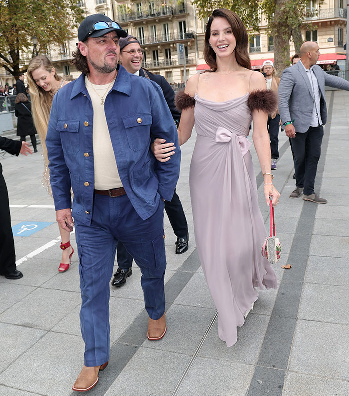 Lana Del Rey and husband walking outdoors, with husband praised for being classier after Meghan Markle backlash.