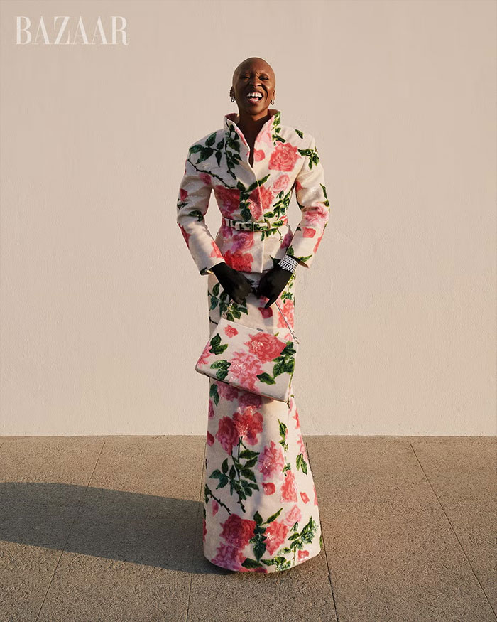 Cynthia Erivo in floral patterned coat dress and matching bag posing for controversial Harper’s Bazaar shoot outdoors.