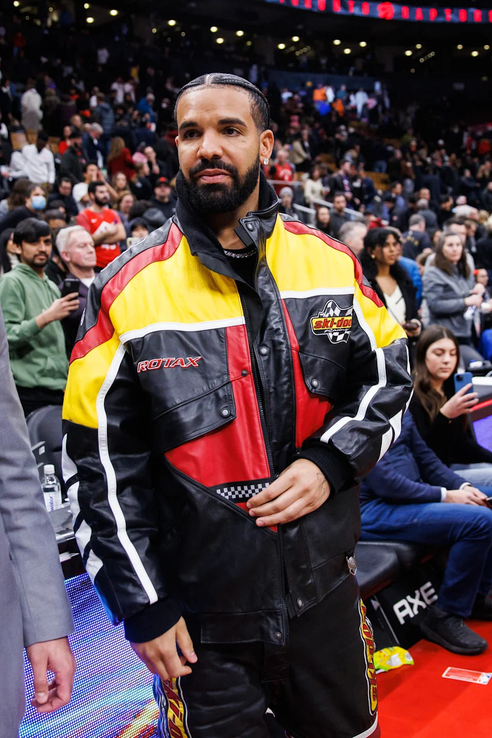 Person in a stylish racing-themed jacket attends an indoor event. Crowd in background