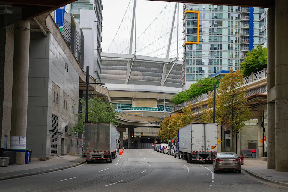 Urban street scene with trucks parked alongside high-rise buildings and a large stadium in the background