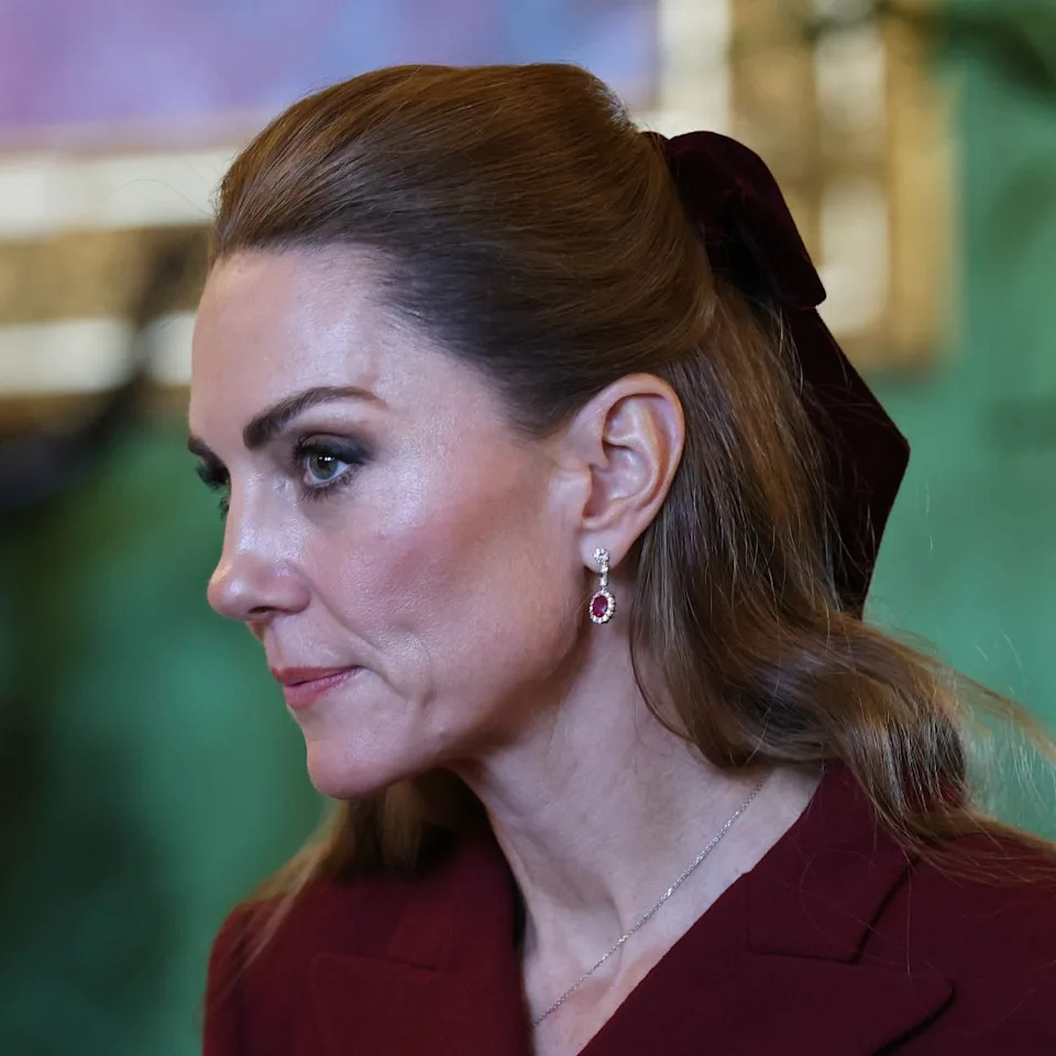  Princess Kate in a burgundy coat and hair bow looking serious . 