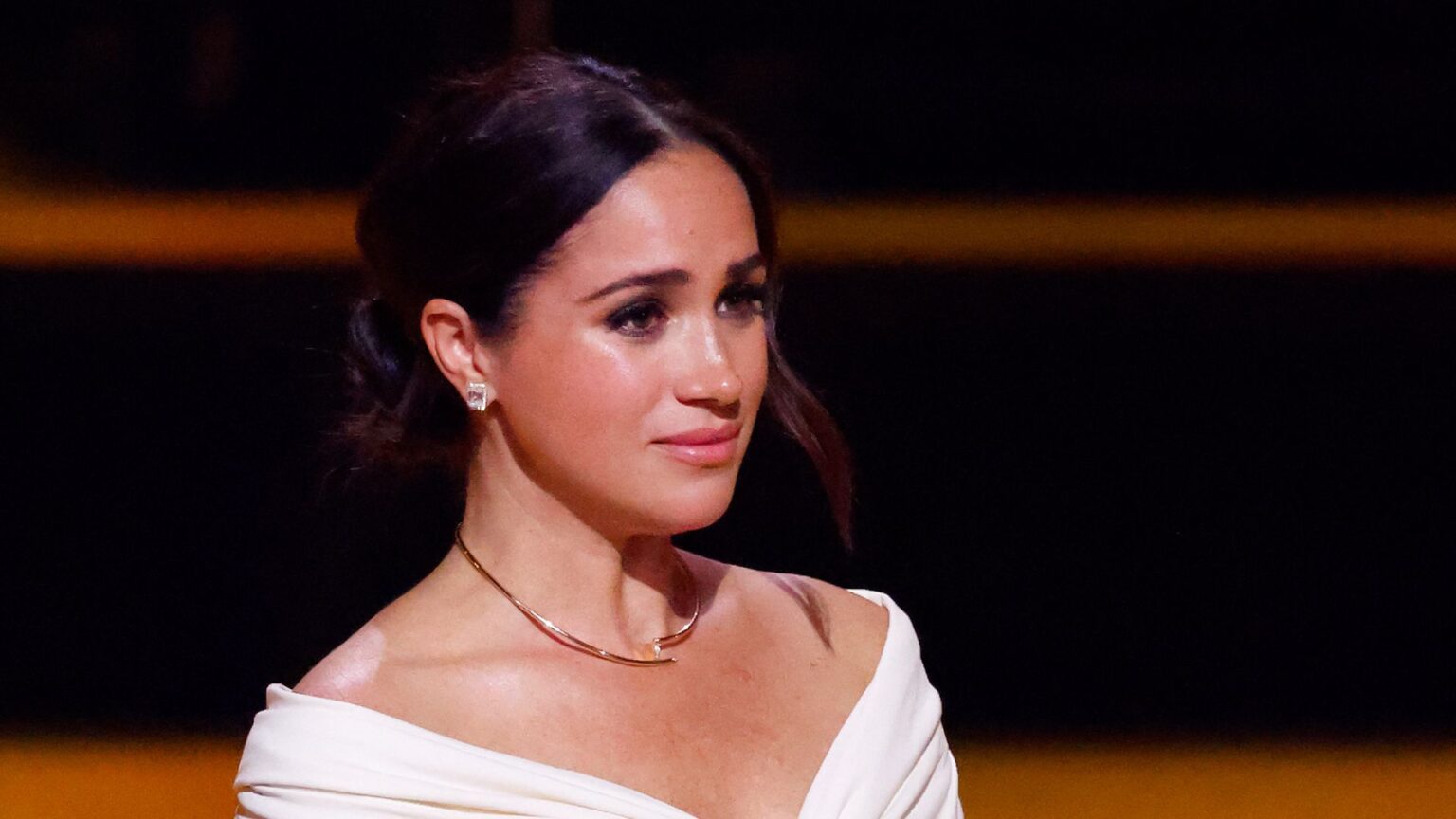 Meghan Markle looks tearful at an event while wearing a white top
