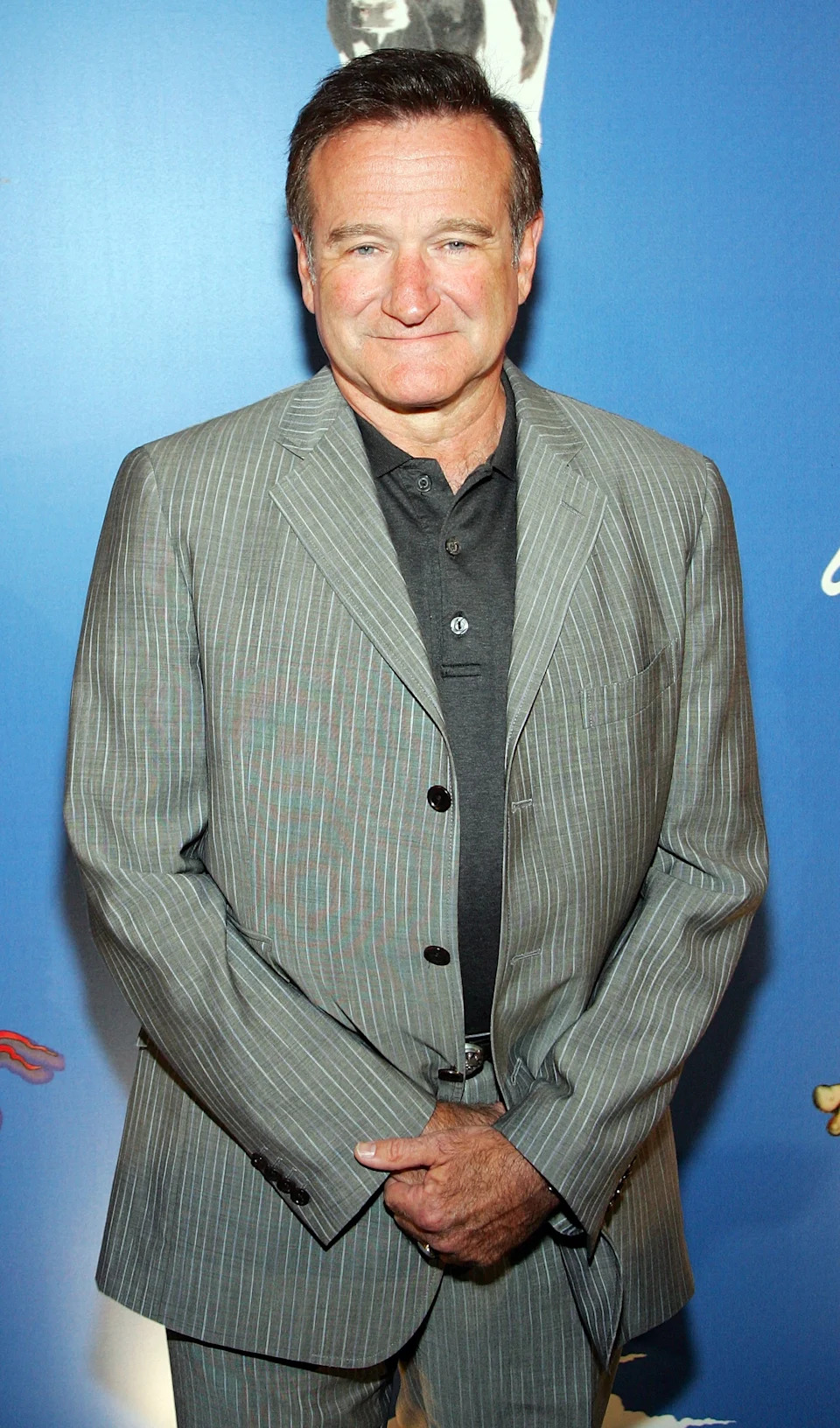Person in a pinstripe suit with a buttoned shirt standing against a blue backdrop, attending a formal event