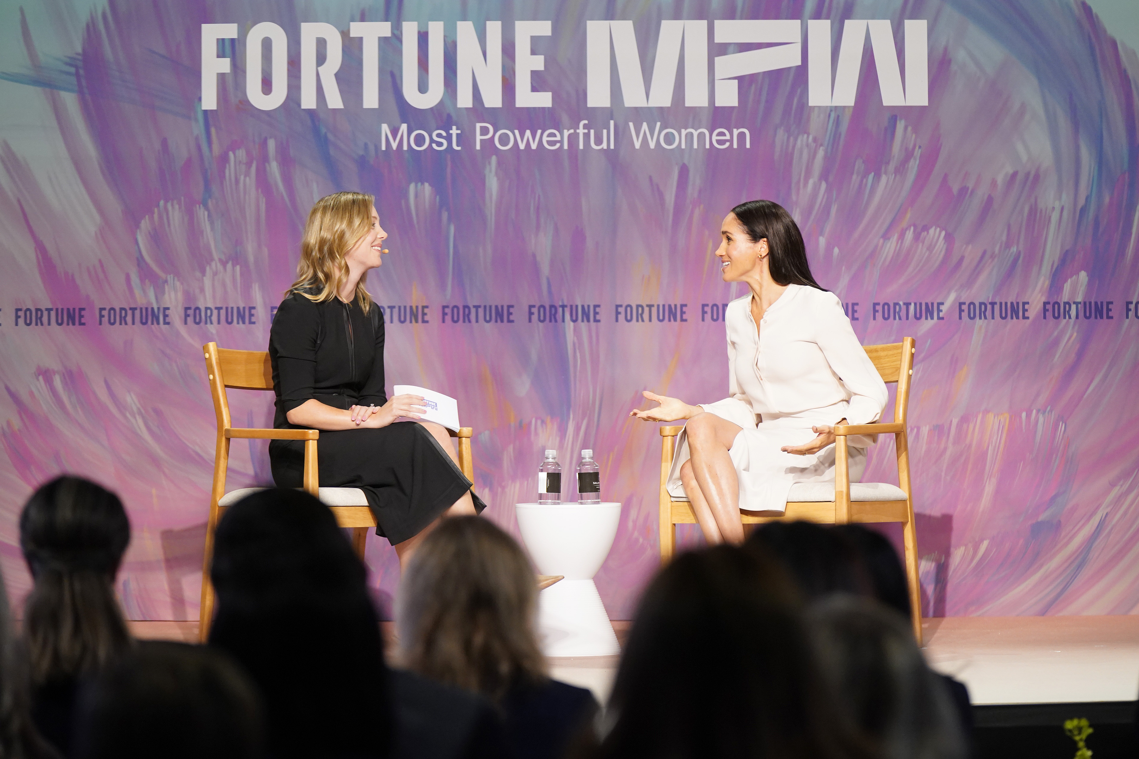 Alyson Shontell and Meghan Markle sitting on stage talking to each other in front of a purple background