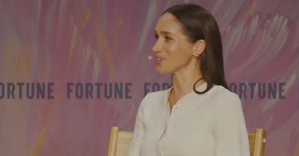 Meghan Markle at the Fortune Powerful Women summit on stage, seated, with an ear microphone.