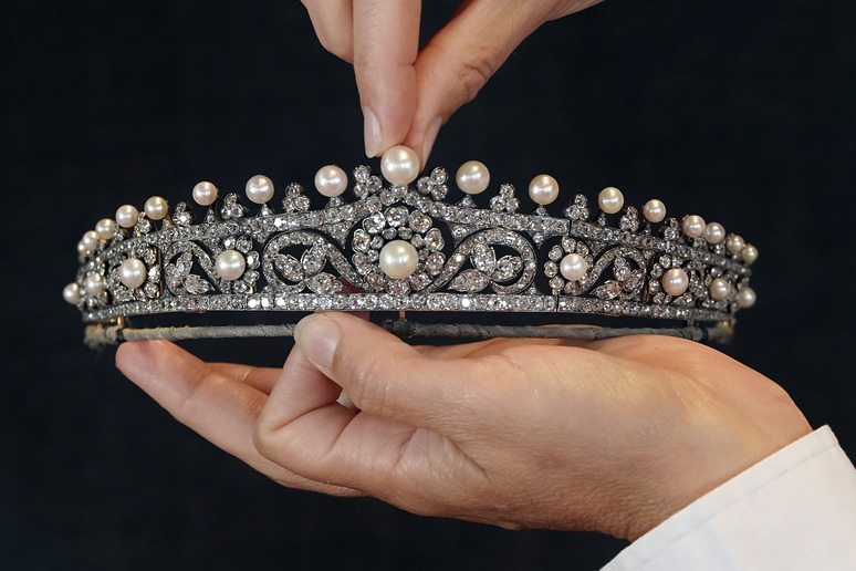Hands holding a tiara adorned with pearls and diamonds on a dark background.