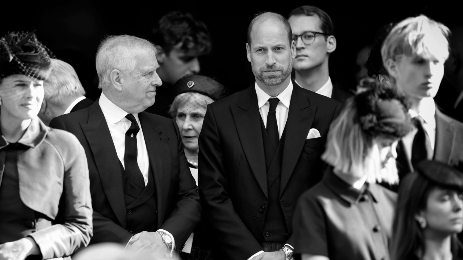 Prince William, wearing a black suit at Duchess of Kent's funeral, looking serious as Prince Andrew turns to smile at him
