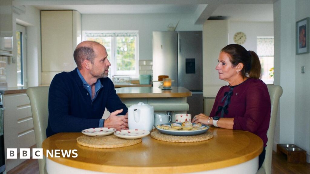 Cardiff widow Rhian Mannings says Prince William’s visit ‘a whirlwind’ Prince Williams and Rhian Mannings sat around her kitchen table talking with a cup of tea. On the table there is a tea pot, two heart patterned plates and a plate of Welsh cakes. Williams, on the left, wears a navy quarter zip and a light blue shirt. On the right, Rhian wears a long sleeved burgundy blouse with black bow details. She has dark brown hair in a ponytail.