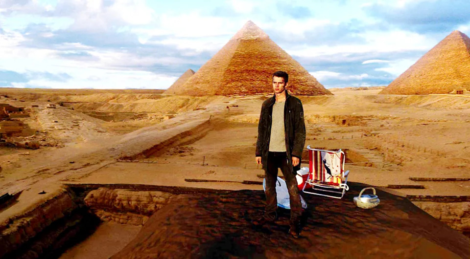 Person standing in front of the Pyramids of Giza with a folded chair and basket nearby