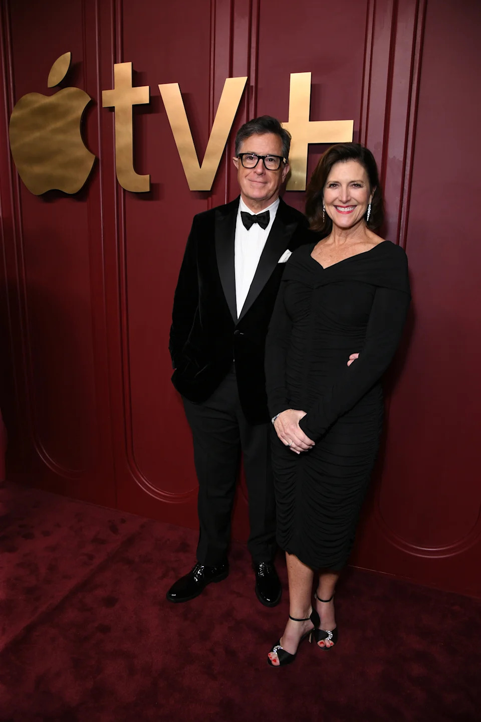 Stephen Colbert and Evelyn McGee-Colbert in formal attire on a red carpet with an Apple TV+ backdrop