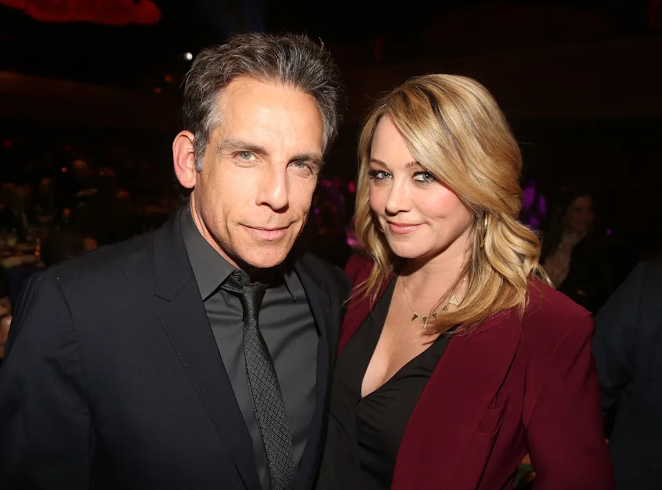 Ben Stiller in a black jacket smiles next to wife Christine Taylor in a black shirt and crimson jacket