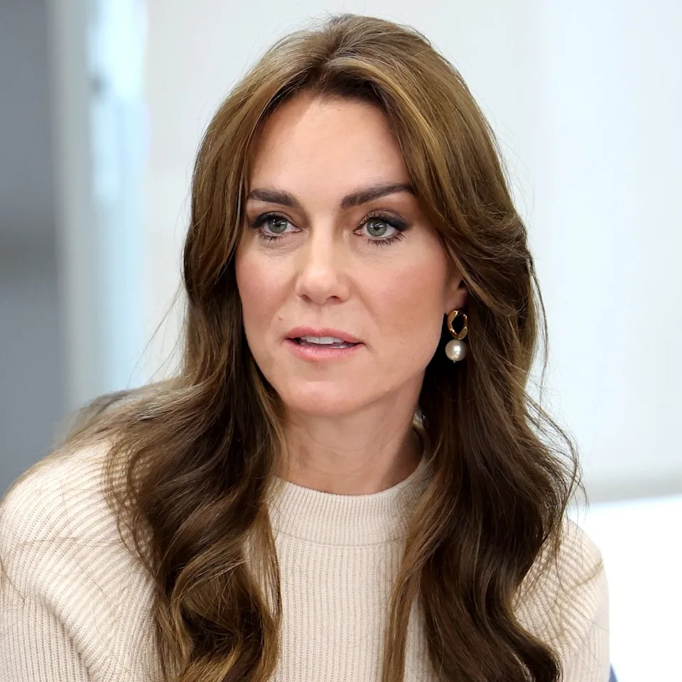  Kate Middleton has long brown hair and wears a cream sweater. 
