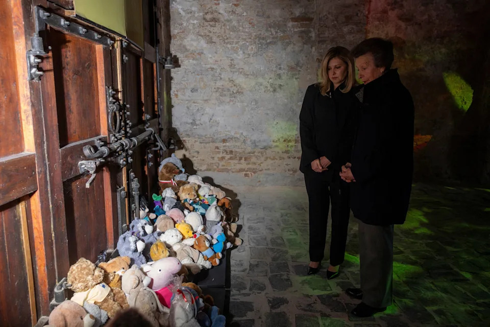 Princess Anne and First Lady Olena Zelenska wearing dark coats, viewing a monument to children filled with teddy bears 