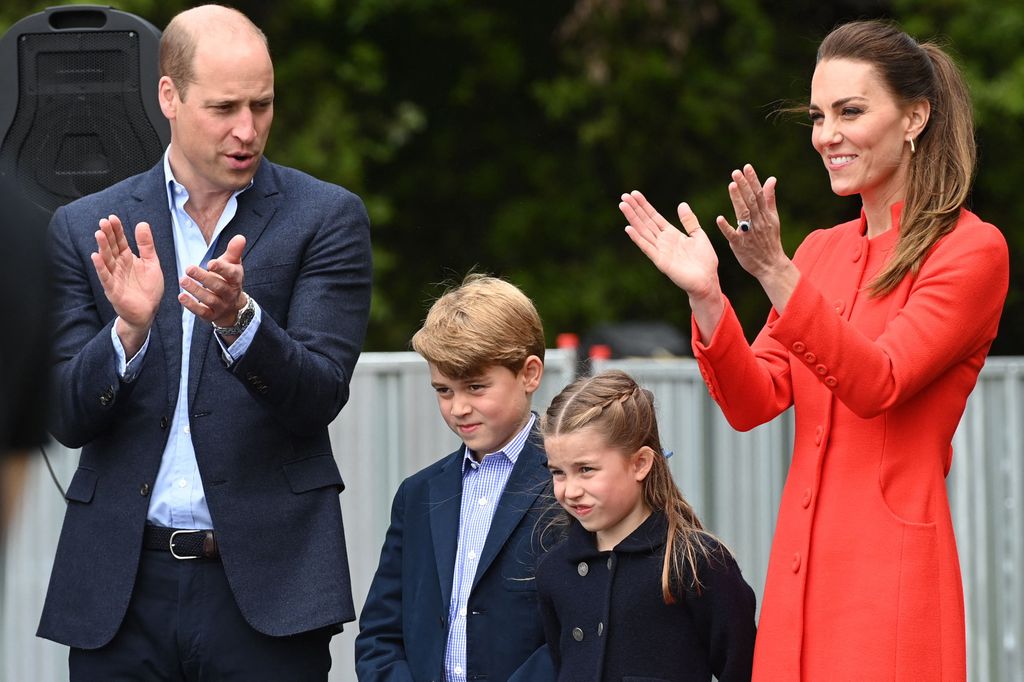 Prince William in suit and Catherine in red coat with george and charlotte clapping