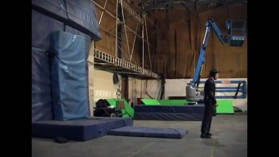 A person standing on a film set with padding walls and a large boom lift in the background