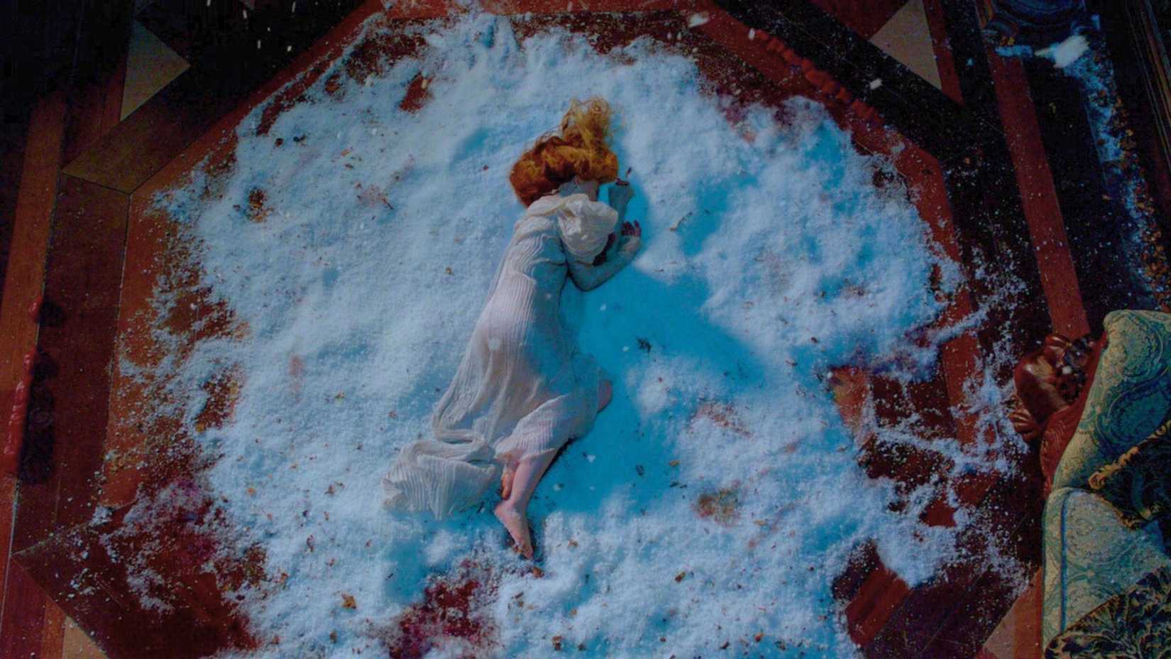 Screenshot from Crimson Peak. It shows Edith, in a white dress, on the floor where a pile of snow is. She's bare foot and injured.