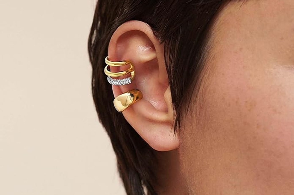 An ear adorned with three gold ear cuffs. One cuff is plain, the middle cuff has diamonds, and the third is a thick gold ring.