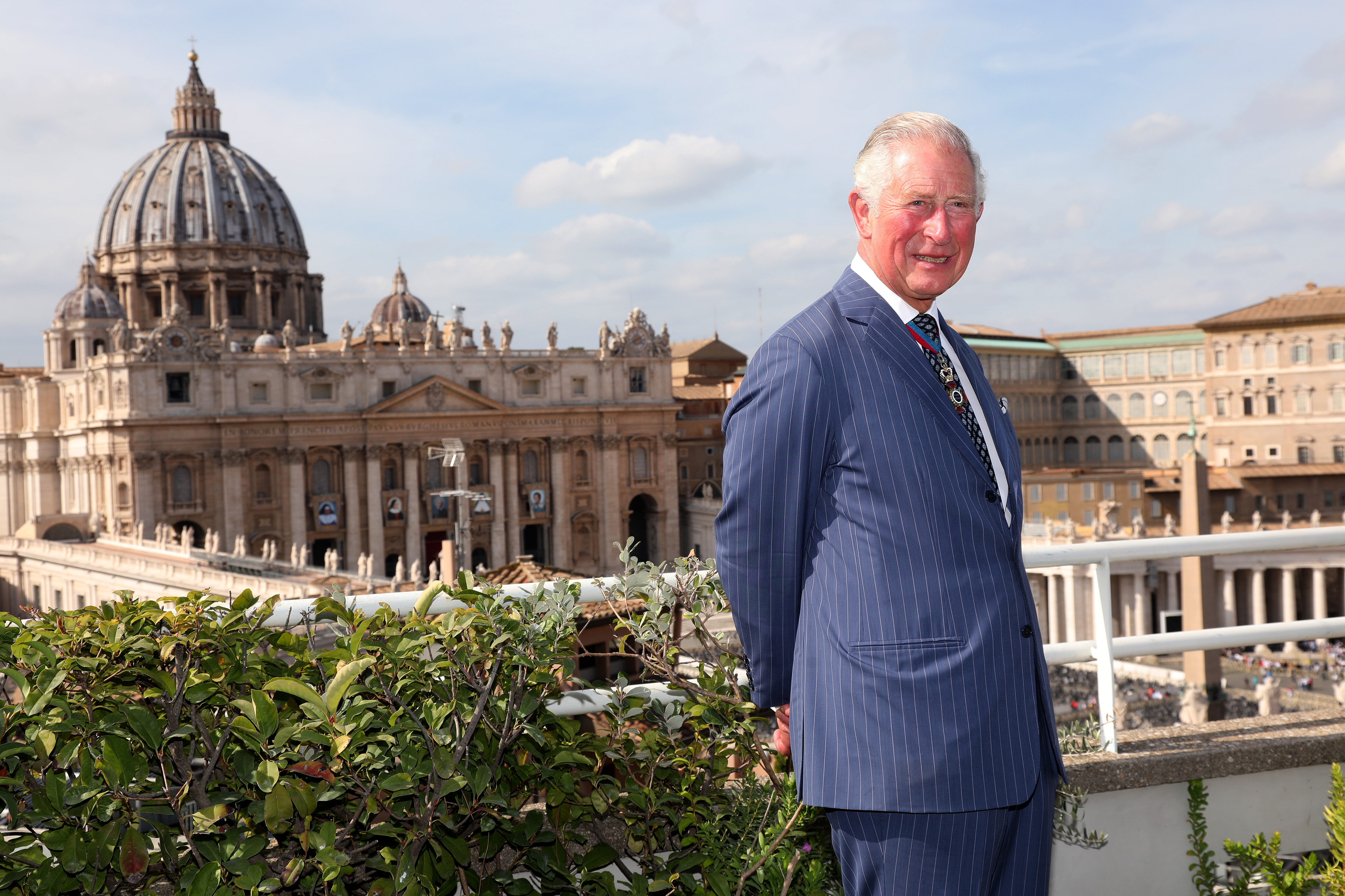 King Charles wearing a blue suit in front of St Peter's basilica