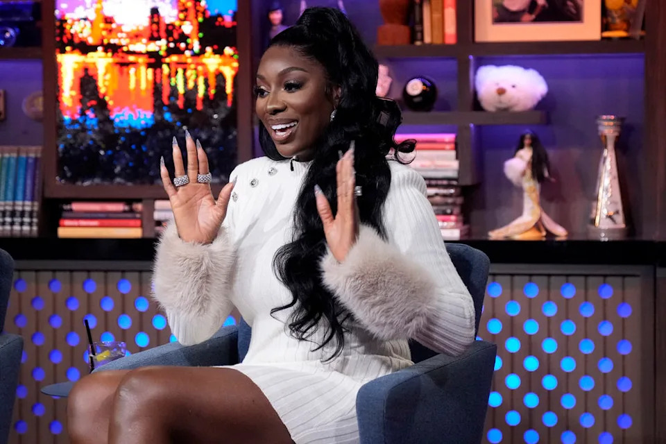 Wendy Osefo raising her hands and wearing a white dress on Watch What Happens Live