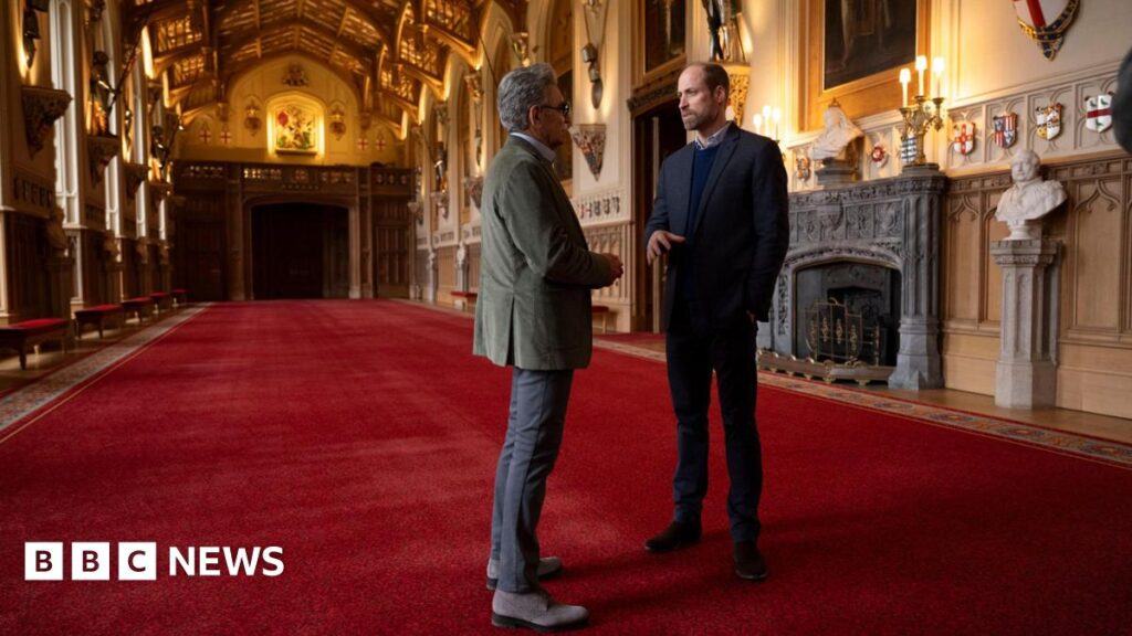 Prince William showing Eugene Levy inside Windsor Castle, they are in a large room or corridor with red carpet and ornate furnishings
