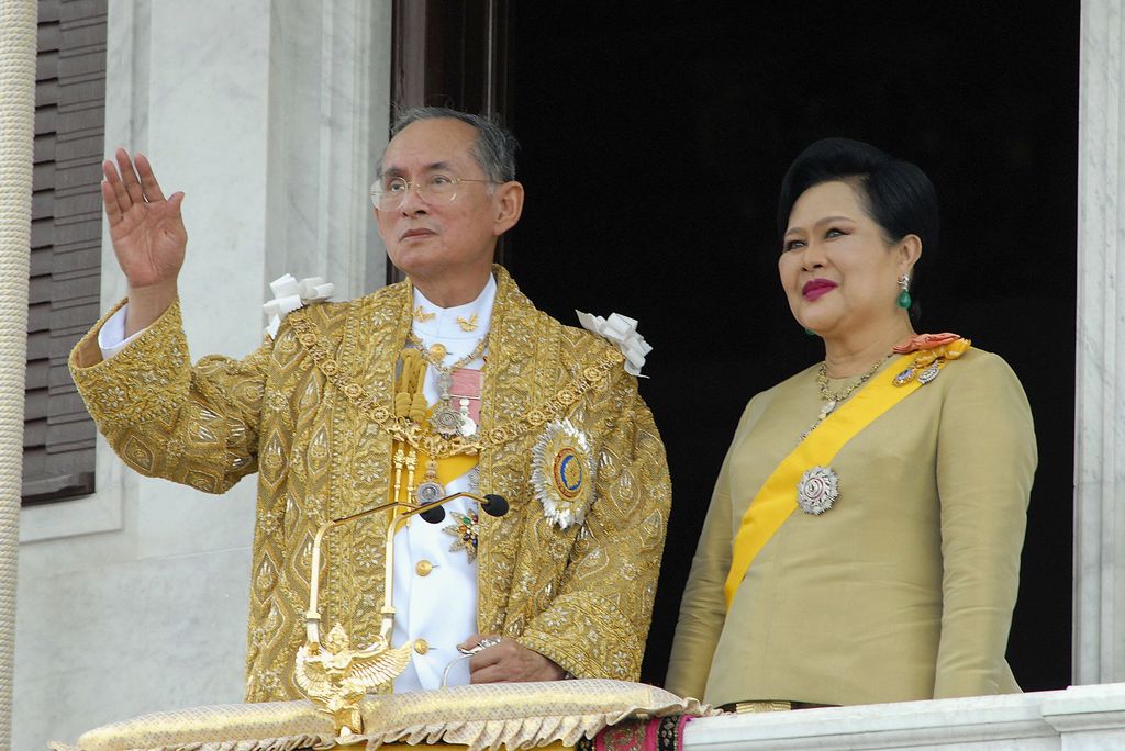 Thailand's King Bhumibol Adulyadej and Queen Sirikit wave to the thousands of people waiting outside the Royal Plaza to pay tribute to King Bhumibol Adulyadej on June 9, 2006 