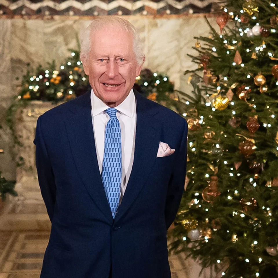  King Charles standing in front of a Christmas tree in a blue suit and tie. 