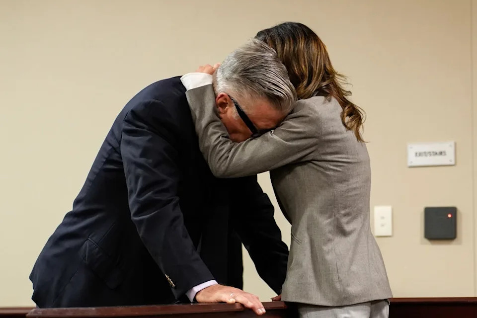 Two people share an emotional embrace in a courtroom setting, showing support and comfort during a serious moment