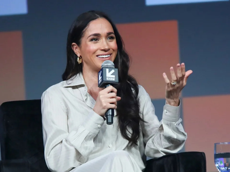 Meghan gestures to the crowd while speaking onstage