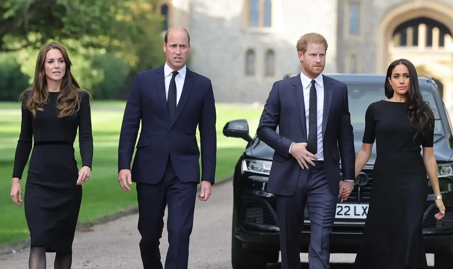 Prince William, Princess Catherine, Prince Harry, and Meghan Markle walking together at Windsor Castle, dressed in black formal attire during a public appearance.