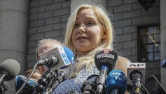 A blonde woman with a bank of microphones in front of her.