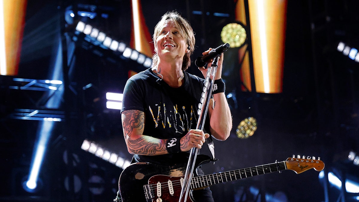 Keith Urban performing on the main stage at Nissan Stadium during CMA Fest 2025, smiling and holding his mic stand.